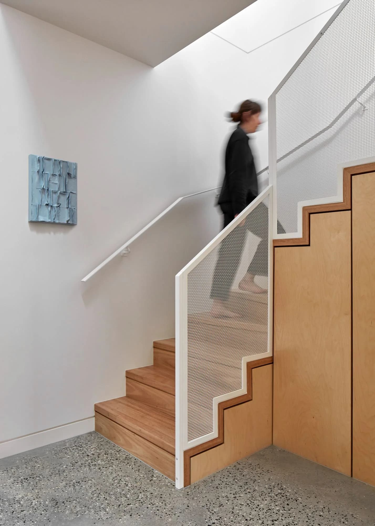 Plywood stair with white perforated balustrade and terrazzo floor below