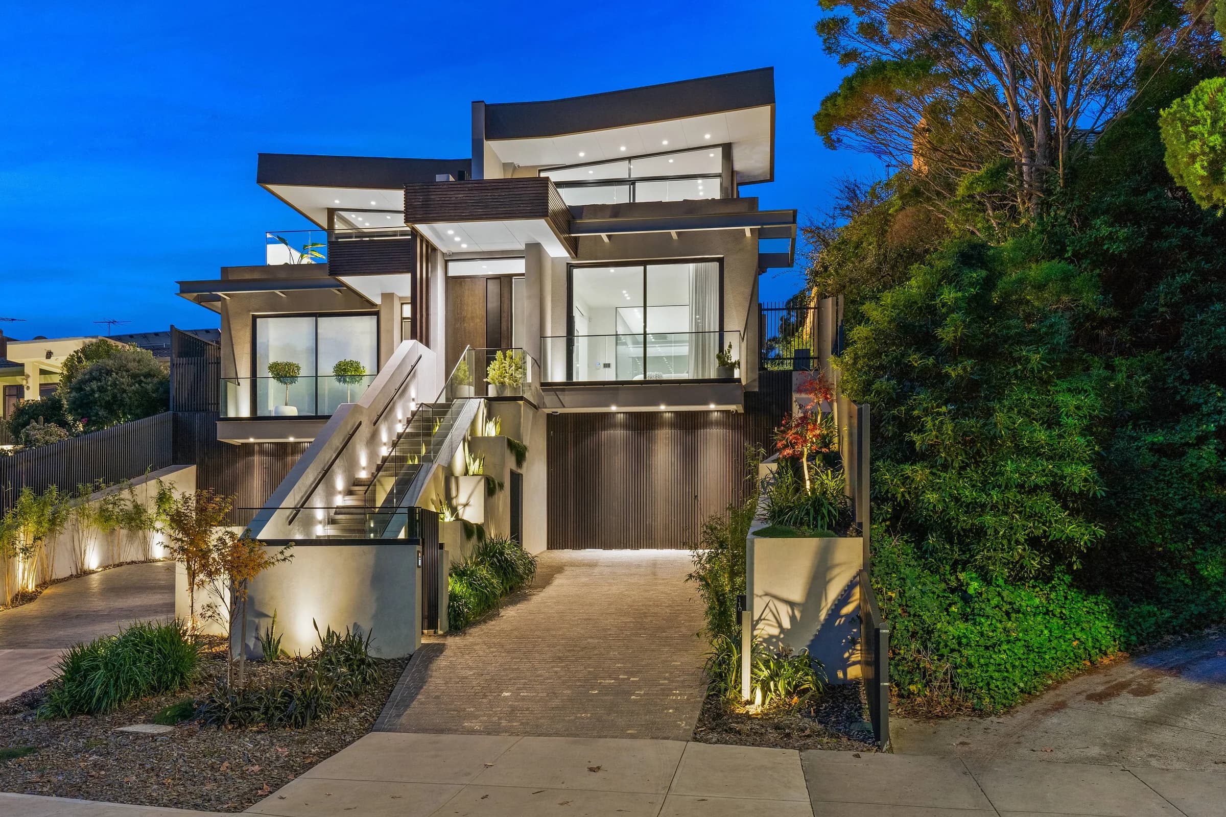Two-storey rebuilt home at dusk with landscaped drive and exterior lighting