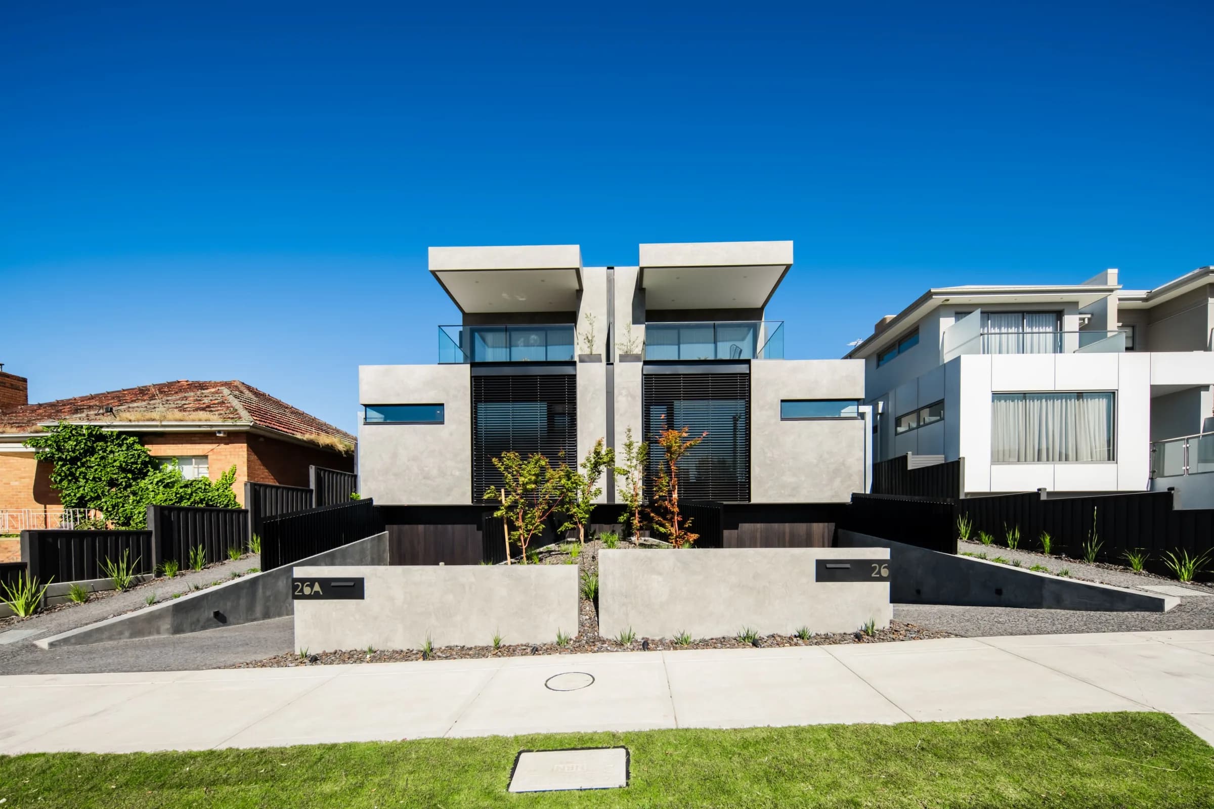 Twin three-storey duplex with cantilevered upper floors under a clear blue sky