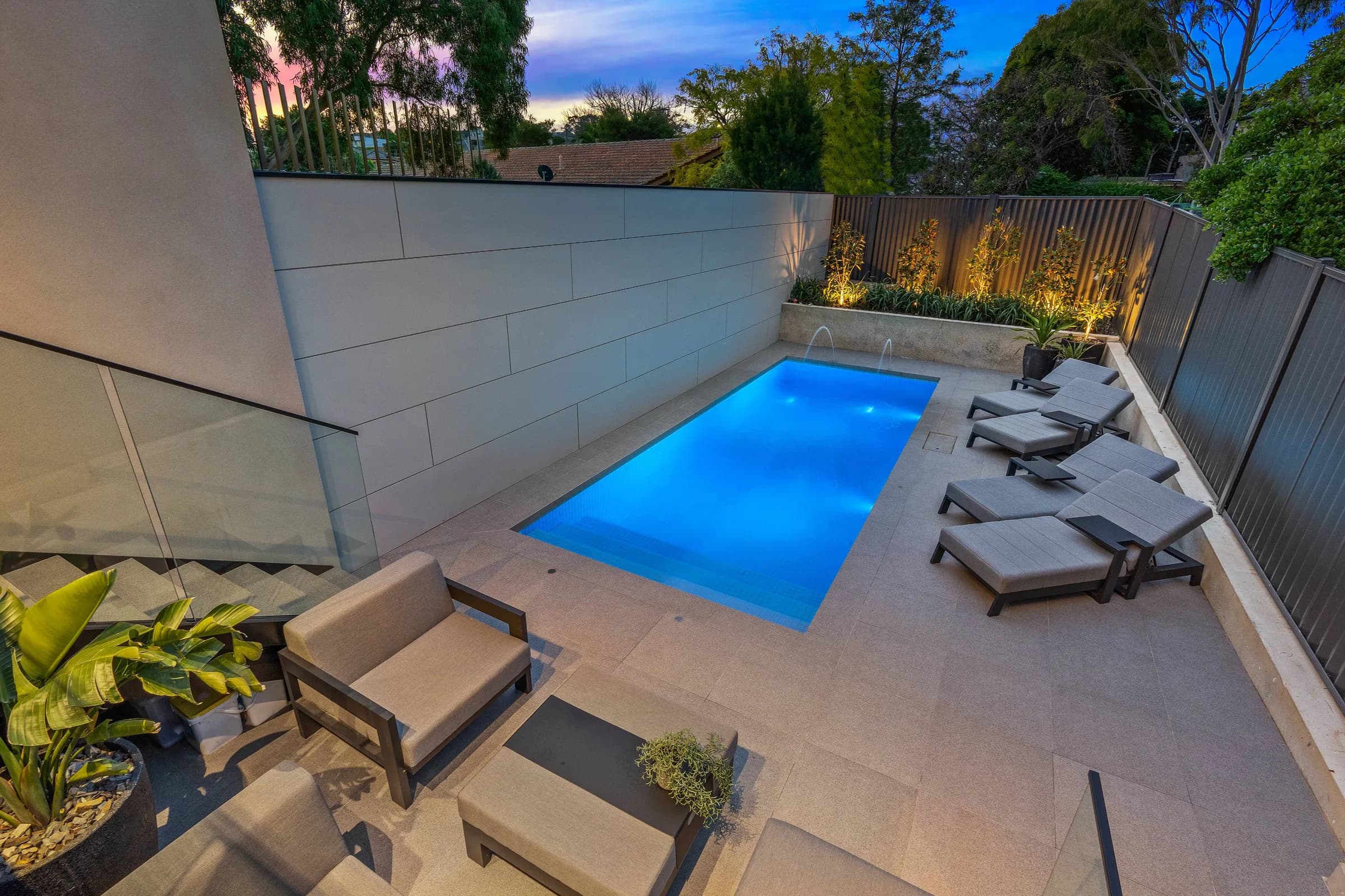 Pool courtyard at dusk with lounging deck and rendered boundary wall
