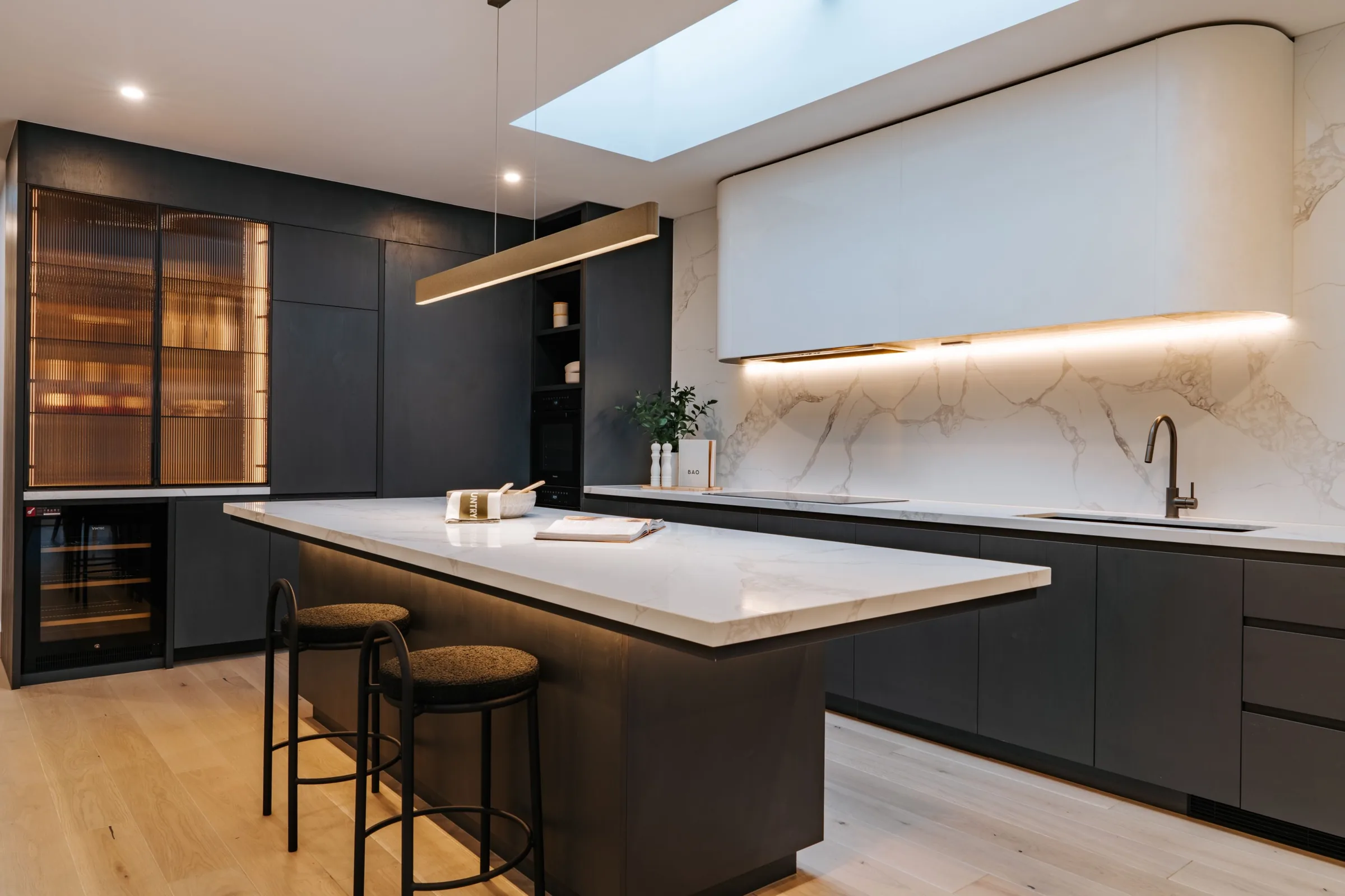 Long dark kitchen island under a ridge skylight with city glimpse